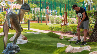 Uomo gioca a minigolf al Valamar Camping Lanterna in Istria, Croazia, accanto a una statua di dinosauro.