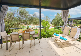 Overdekt terras bij Premium Holiday Home op Aminess Planet Camping Sirena met stoelen, tafel en ligstoelen.