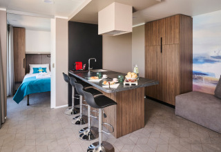 Luxe vakantiewoning met moderne keuken, barkrukken en uitzicht op een stijlvolle slaapkamer.