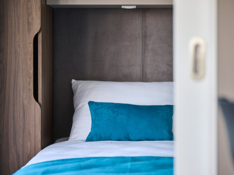 Knusse slaapruimte met wit beddengoed en turquoise kussen in een luxe vakantiehuis op Aminess Planet Camping Sirena, Kroatië.