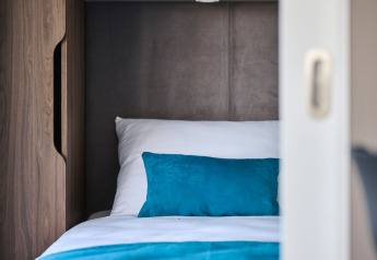 Gezellige slaapruimte met wit beddengoed en turquoise kussen in een luxe chalet op Aminess Planet Camping Sirena, Kroatië.