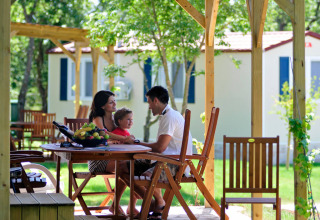 Famiglia seduta a un tavolo di legno davanti a lodge glamping immersi nella natura verdeggiante.
