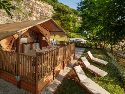 Tienda de glamping de lujo con cocina, terraza de madera y tumbonas en un hermoso entorno natural.