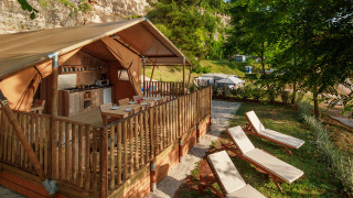 Tienda de glamping de lujo con cocina, terraza de madera y tumbonas en un hermoso entorno natural.