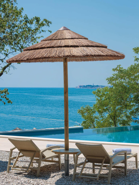 To liggestole under en stråparasoll ved poolen med udsigt over havet ved Valamar Camping Lanterna, Kroatien.
