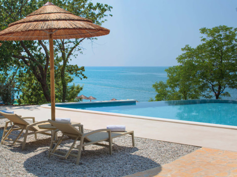 Lettini e ombrellone in paglia accanto alla piscina a sfioro con vista mare in tenda safari.