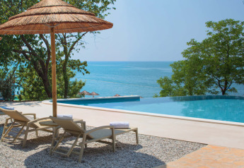Transats et parasol en paille au bord de la piscine avec vue sur mer depuis une tente safari de luxe.