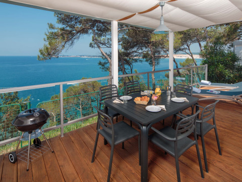Terrasse im Lanterna Home Seaside Chalet mit Meerblick, Esstisch, Grill und Holzdeck unter Segeltuch.