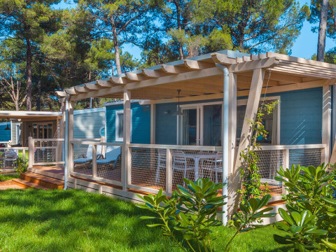 Chalet Marine Home con veranda in legno, tavolo e sedie bianche all'aperto, immerso nel verde e tra pini.