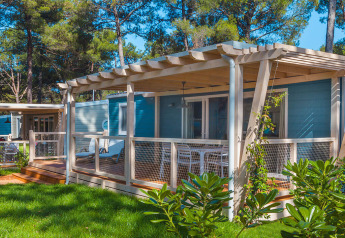 Marine Home chalet met houten terras en tuinmeubilair, omgeven door fris groen gras en hoge bomen.