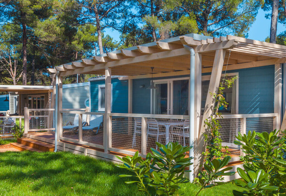 Chalet Marine Home con veranda in legno, tavolo e sedie bianche all'aperto, immerso nel verde e tra pini.