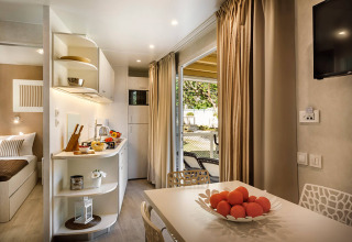 Hébergement glamping moderne avec coin repas, cuisine, corbeille de fruits et accès à la terrasse extérieure.