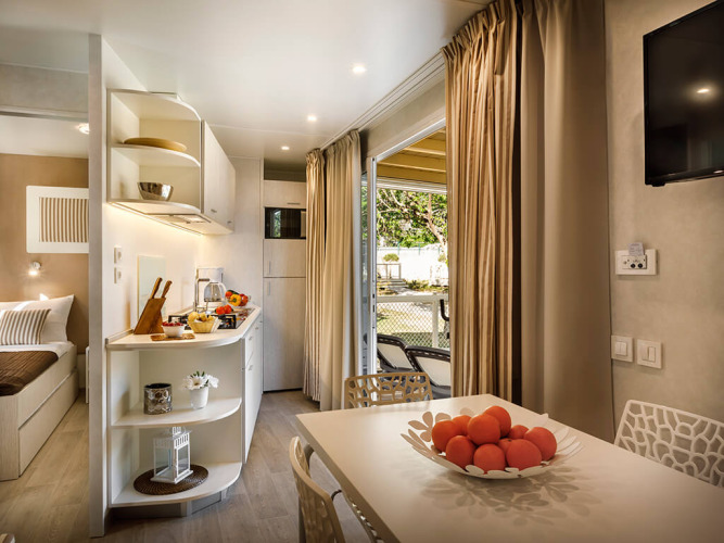 Hébergement glamping moderne avec coin repas, cuisine, corbeille de fruits et accès à la terrasse extérieure.