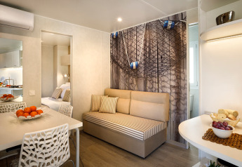 Hyggelig glampingbolig med moderne sofa, spisebord og friske frugter, inspireret af maritim stil.
