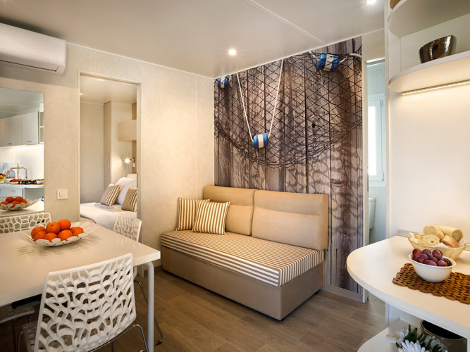 Accogliente sistemazione glamping con divano a righe, tavolo da pranzo e decorazioni nautiche.