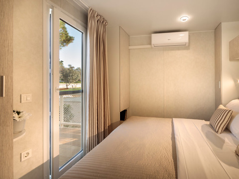 Hébergement glamping moderne avec lit confortable, climatisation et vue sur la nature à travers la porte vitrée.