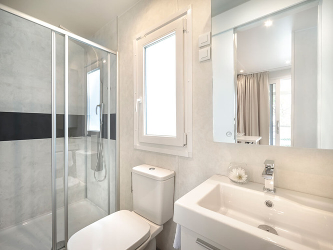 Baño moderno en un alojamiento glamping con ducha, ventana, inodoro y lavabo con espejo amplio.