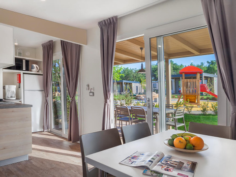 Moderne chalet interiør med spisebord, køkken og udsigt over legeplads i Valamar Camping Lanterna, Kroatien.