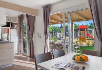 Moderne chalet interiør med spisebord, køkken og udsigt over legeplads i Valamar Camping Lanterna, Kroatien.