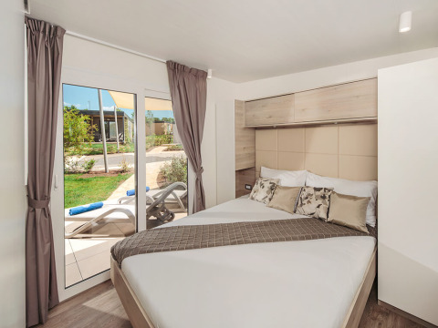 Soveværelse i Mediterranean Garden Home chalet på Valamar Camping Lanterna med udsigt til terrasse.