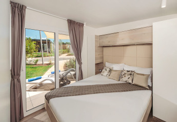 Soveværelse i Mediterranean Garden Home chalet på Valamar Camping Lanterna med udsigt til terrasse.