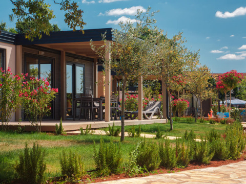 Udsigt til moderne Mediterranean Garden Home chalet med grøn have, blomster og havemøbler om sommeren.
