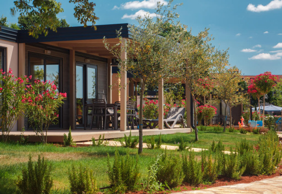 Udsigt til moderne Mediterranean Garden Home chalet med grøn have, blomster og havemøbler om sommeren.