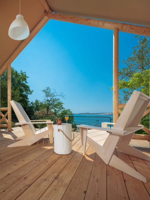 Houten terras met stoelen en tafel, uitzicht op de zee vanuit een Glamping Superior Tent bij mooi weer.
