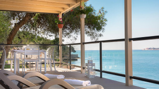 Terrasse des Marbello Home Chalets mit Blick aufs Meer, Liegestühlen und Essbereich unter Pergola.
