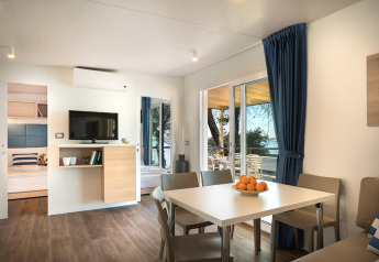 Moderne leefruimte in Marbello Home chalet met eettafel, sofa en zicht op terras en zee.