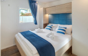 Modernes Glamping-Schlafzimmer mit Doppelbett, blauen Akzenten, Holzfußboden und Fenster.