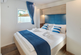 Chambre de glamping moderne avec lit double, touches bleues et blanches, sol en bois et fenêtre.