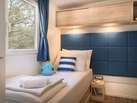 Chambre individuelle confortable au Marbello Home avec coussin rayé, peluche bleue et vue sur la forêt.