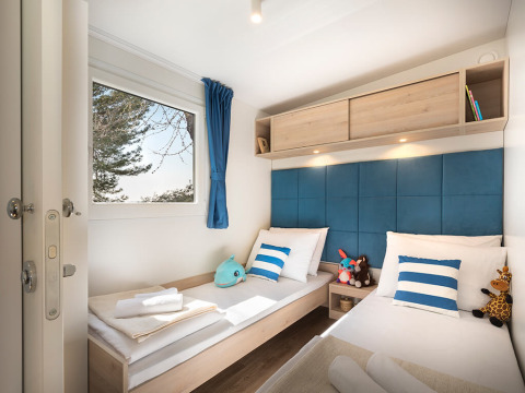 Moderne glampingkamer Marbello Home met twee eenpersoonsbedden, blauw-witte kussens en knuffels, zonlicht binnen.