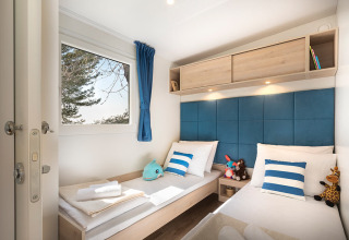 Moderne glampingkamer Marbello Home met twee eenpersoonsbedden, blauw-witte kussens en knuffels, zonlicht binnen.