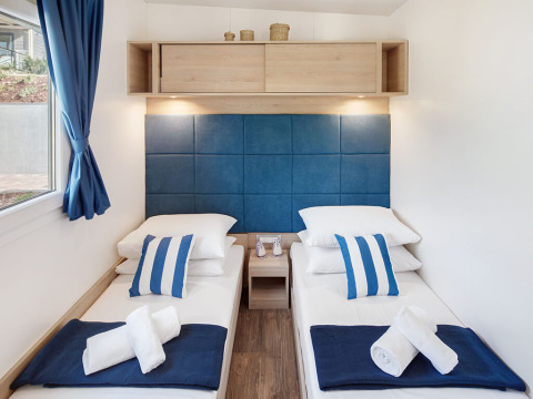 Deux lits simples dans un hébergement glamping avec une tête de lit bleue, des coussins rayés et des serviettes.