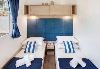 Deux lits simples dans un hébergement glamping avec une tête de lit bleue, des coussins rayés et des serviettes.