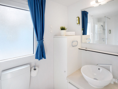 Salle de bain moderne dans un logement glamping avec rideaux bleus, vasque ronde et grand miroir.