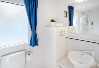 Moderne badkamer in een glampingaccommodatie met blauwe gordijnen, rond wasbakje en grote spiegel.