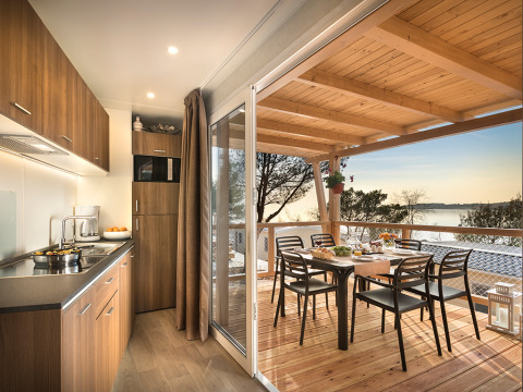 Accogliente lodge Happy Dog Home con cucina aperta, terrazza, vista lago e tavolo apparecchiato all’aperto.
