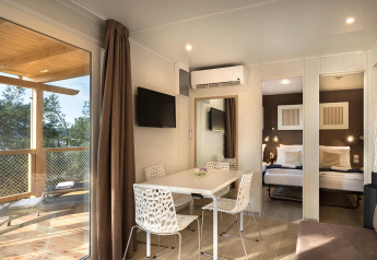 Moderne lodgeinteriør med spisebord, tv og udsigt til terrasse i Happy Dog Home på Valamar Camping Lanterna.