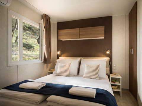 Knusse slaapkamer in Happy Dog Home glamping met tweepersoonsbed, raam en moderne houten inrichting.