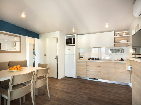 Modern glampingverblijf met open keuken, eettafel, zitbank en licht houten vloerinterieur.