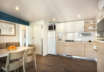 Modern glampingverblijf met open keuken, eettafel, zitbank en licht houten vloerinterieur.