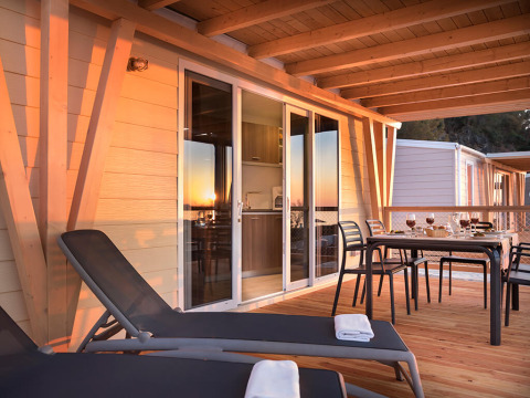 Terras van chalet Happy Dog Home met ligstoelen, gedekte eettafel en houten vloer bij zonsondergang.