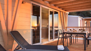 Terrasse des Chalets Happy Dog Home mit Sonnenliegen, gedecktem Tisch und gemütlichem Holzdeck bei Sonnenuntergang.
