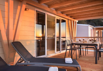 Terras van chalet Happy Dog Home met zonnebedden, gedekte tafel en houten vloer bij zonsondergang.