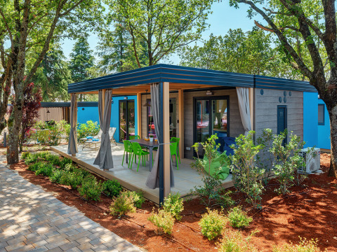 Image of Maro Home chalet surrounded by trees, featuring a covered patio and colorful outdoor chairs.