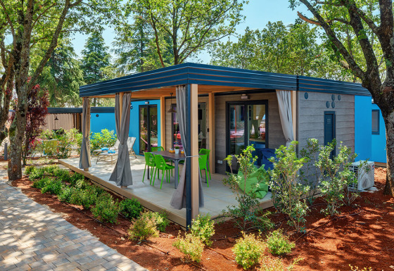 Image of Maro Home chalet surrounded by trees, featuring a covered patio and colorful outdoor chairs.