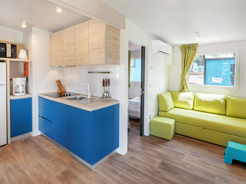 Modern Maro Home chalet at Valamar Camping Lanterna in Croatia with blue kitchen and green sofa shown.
